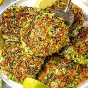 zucchini fritters on a white plate with lemon wedges