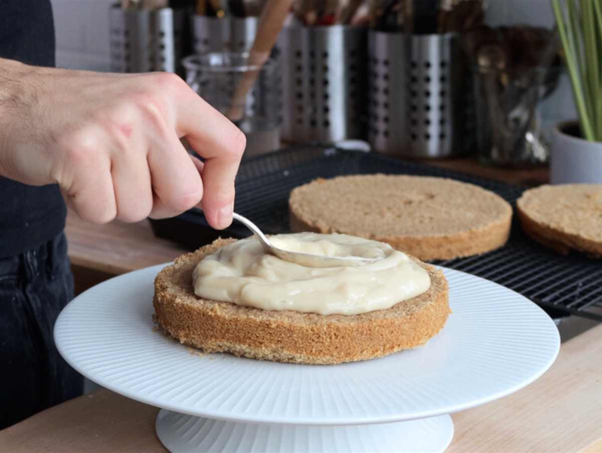 hand applying vegan custard on the vegan coconut cake