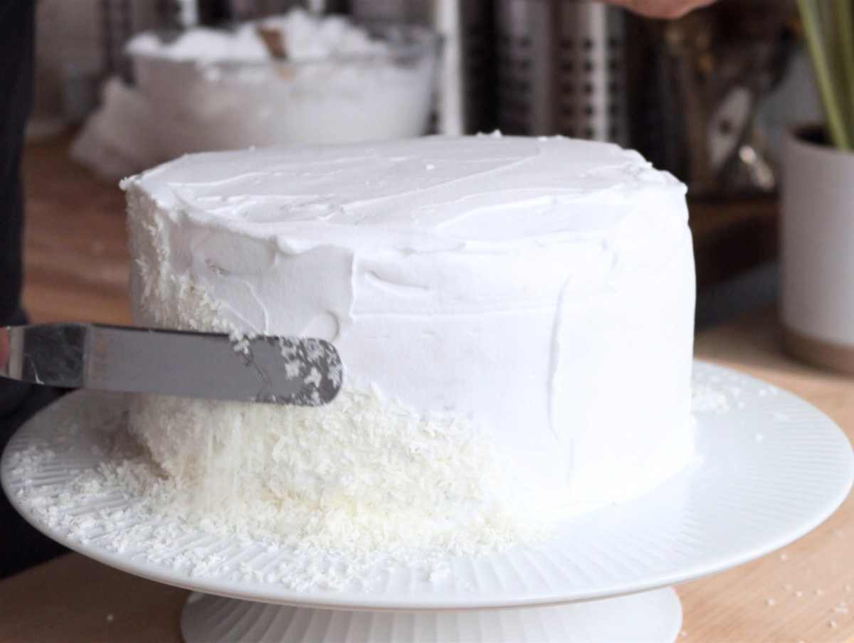 applying vegan whipped cream on the vegan coconut cake