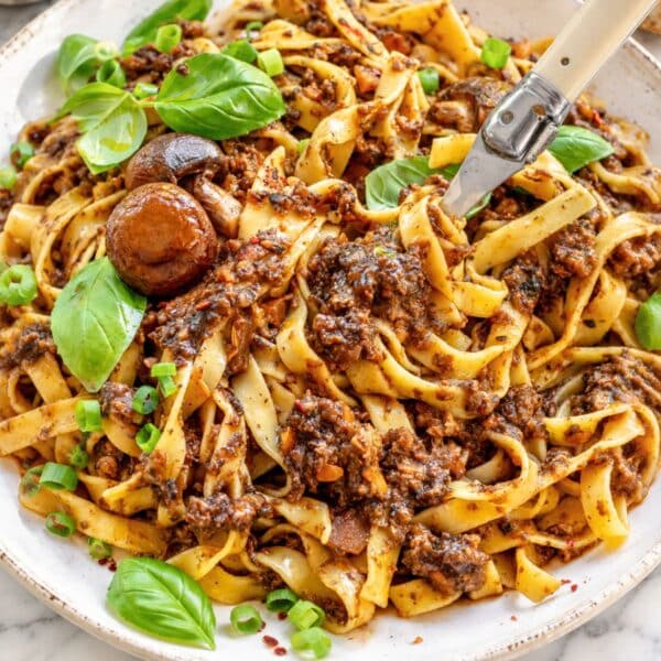 Fettuccine with rich mushroom ragu, basil, and parmesan on white marble.