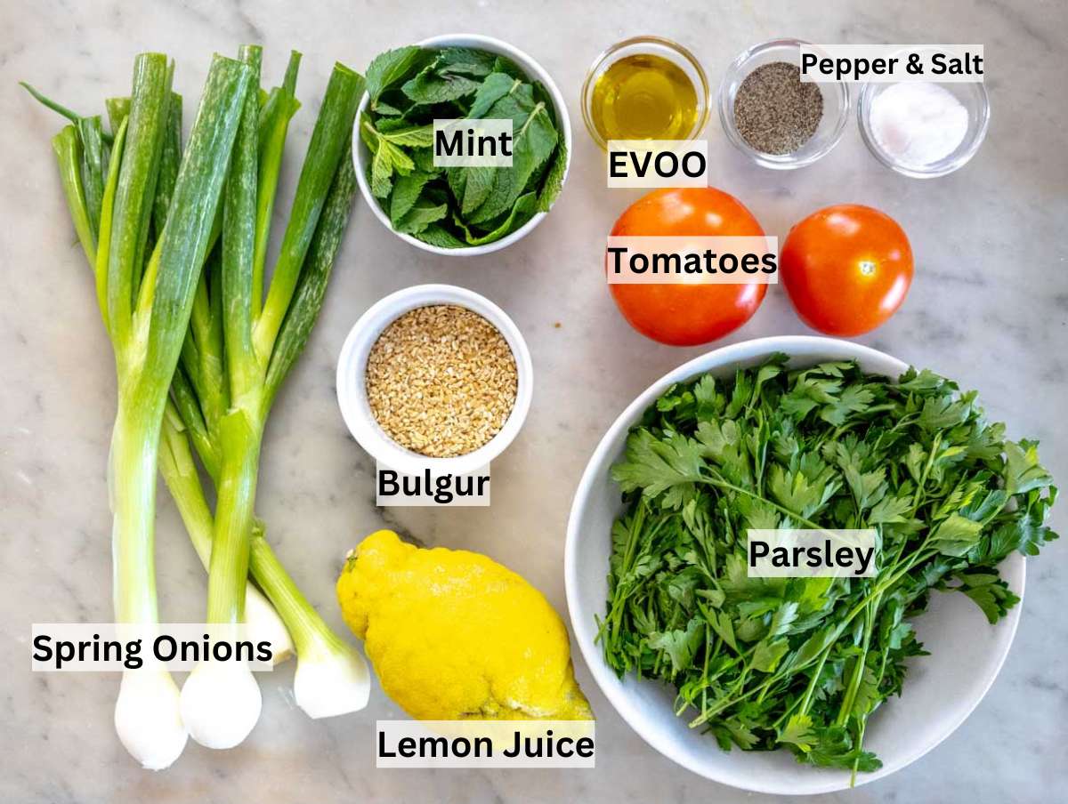 Flat-lay of tabouli (tabbouleh) ingredients parsley, bulgur, tomatoes, mint, scallions, lemon, and olive oil, on a rustic board.