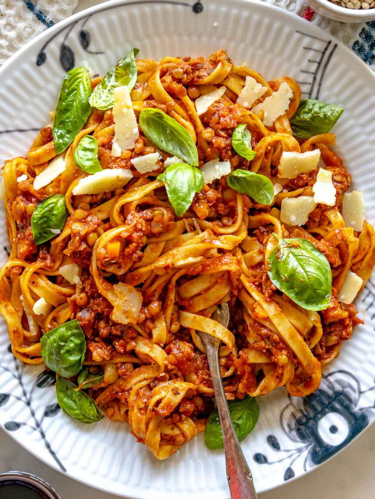 Lentil Bolognese tossed with pasta and finished with grated Parmesan and fresh basil on a marble surface near a bright window.