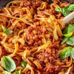 Lentil Bolognese tossed with wide ribbons of pasta and fresh basil, showing the thick tomato sauce with tender lentils and vegetables.