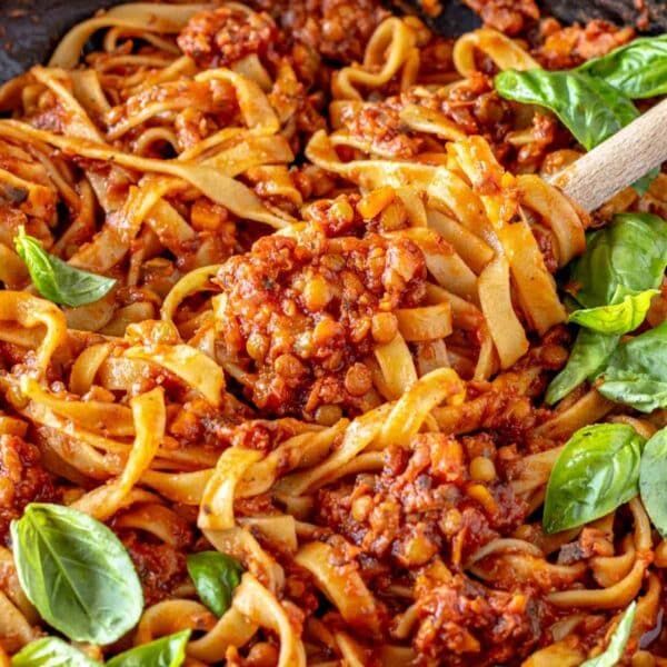Lentil Bolognese tossed with wide ribbons of pasta and fresh basil, showing the thick tomato sauce with tender lentils and vegetables.