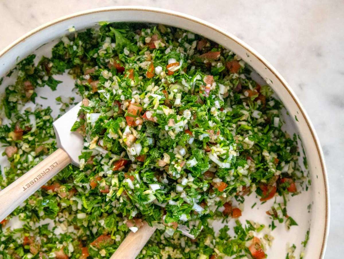 Mixing bowl with tabouli ingredients being tossed with olive oil and lemon juice for a healthy summer salad.