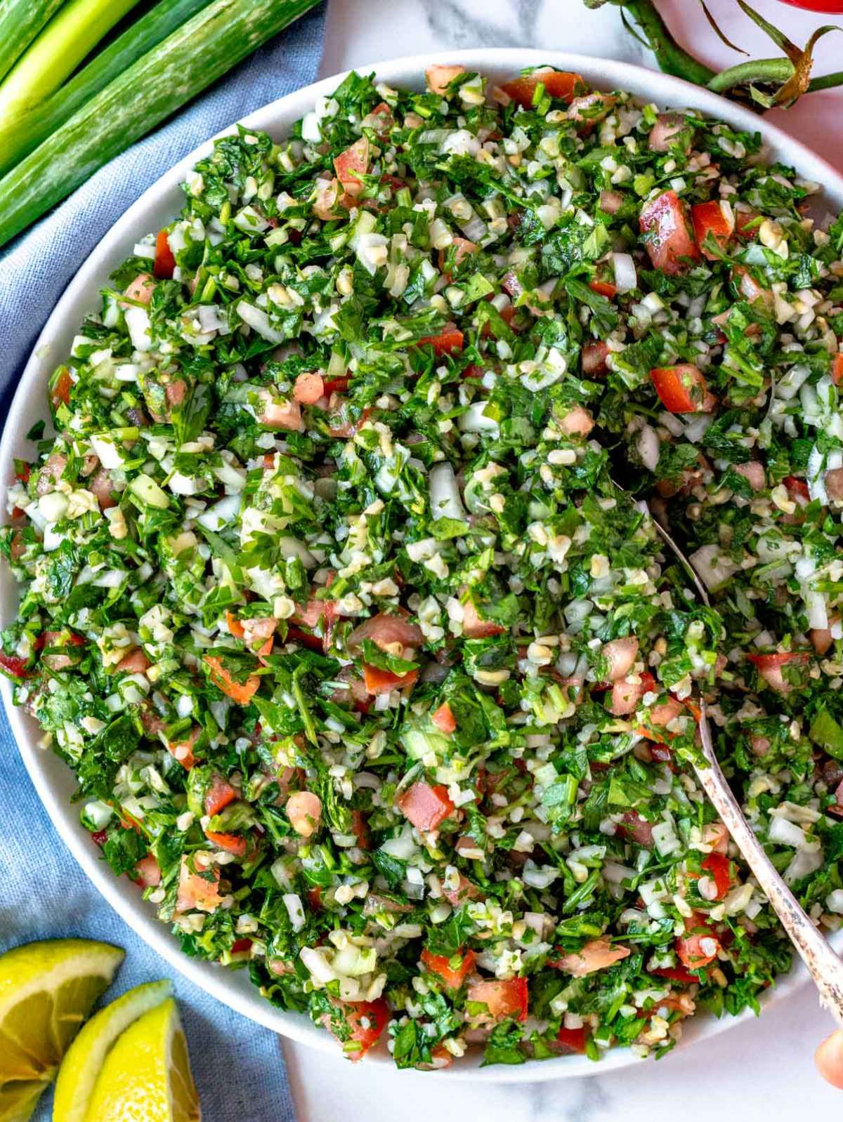 Overhead view of tabouli (tabbouleh) salad served in a white bowl, garnished with lemon slices and romaine lettuce leaves.