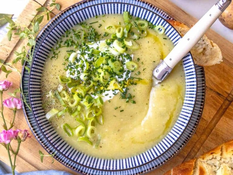 potato leek soup with a white spoon and garlic bread on the side