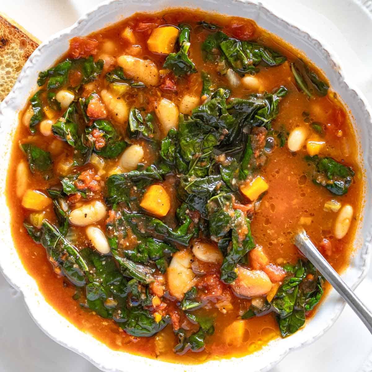 One-pot kale soup with a spoon in a white bowl.