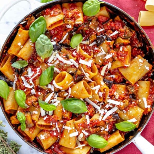 Pasta alla Norma served in a skillet with fresh basil and oregano.