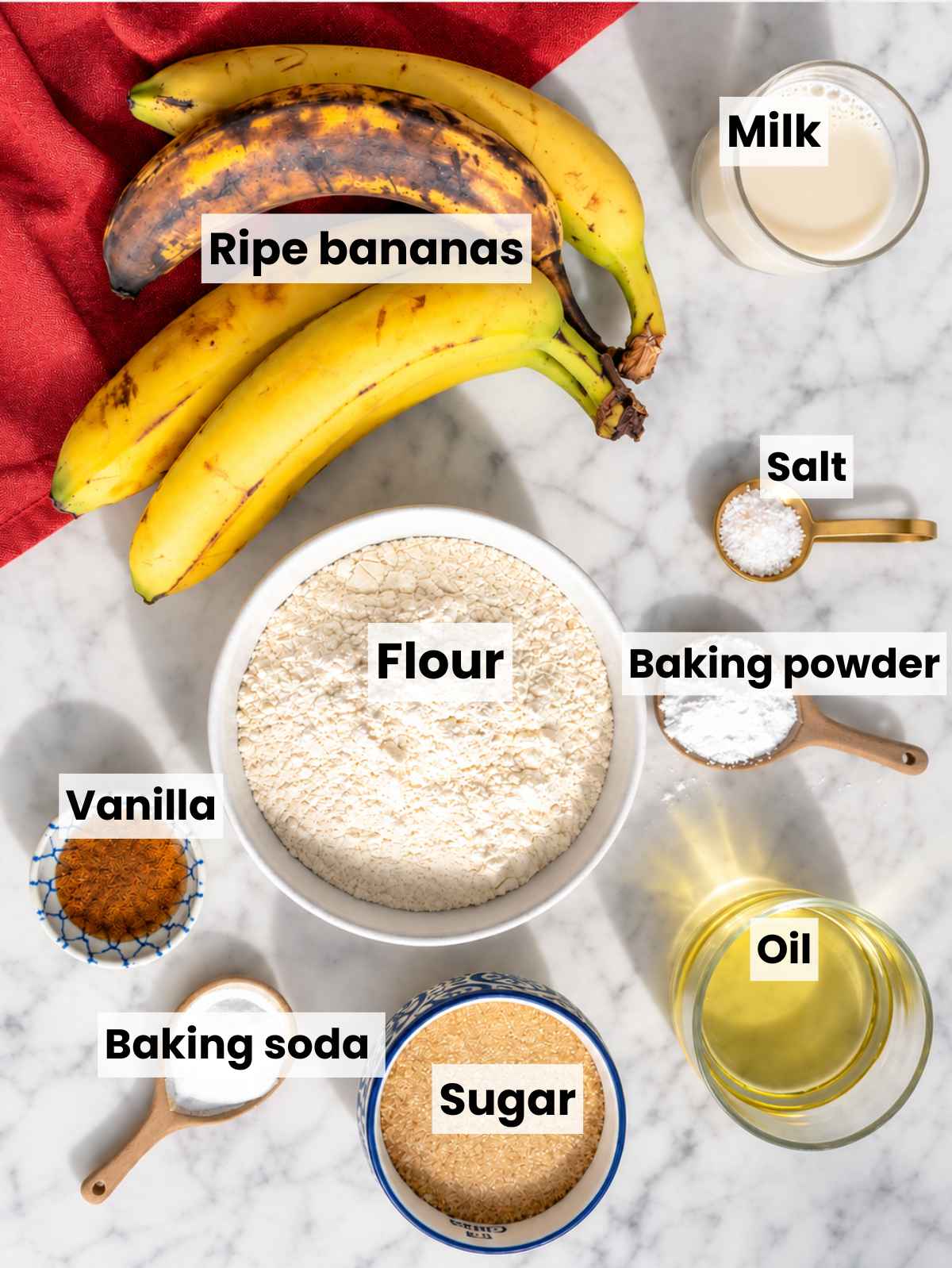 Vegan banana bread ingredients arranged on white marble in natural light.
