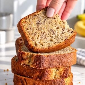 Vegan banana bread sliced thickly on bright white marble and a female hand.