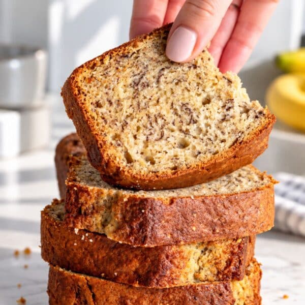 Vegan banana bread sliced thickly on bright white marble and a female hand.