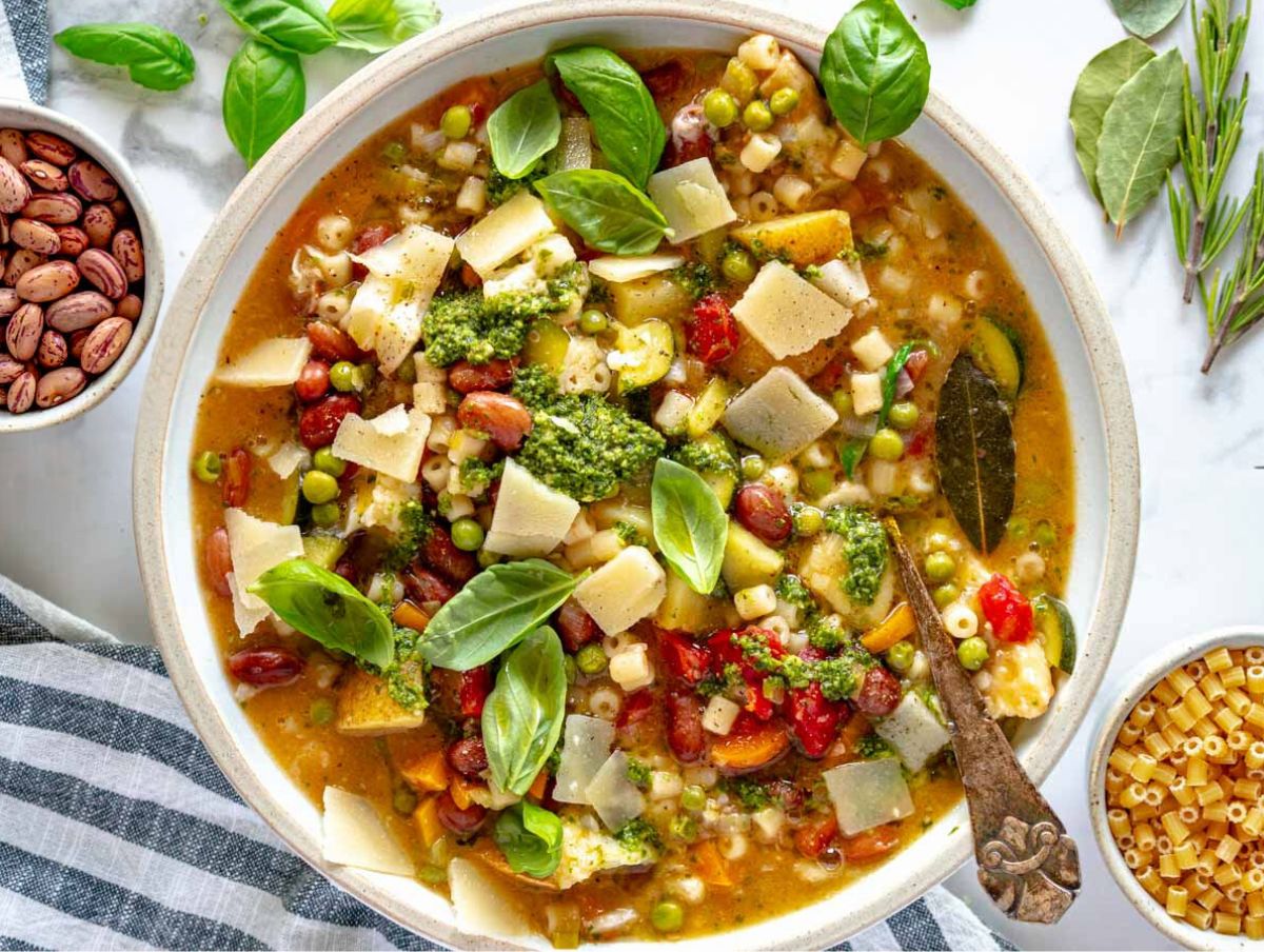 minestrone soup in a bowl topped with pesto, parmesan, and basil