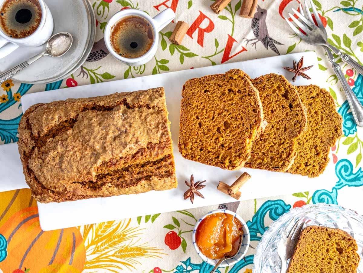 sliced vegan pumpkin bread on a marble cutting board served with coffee and jam