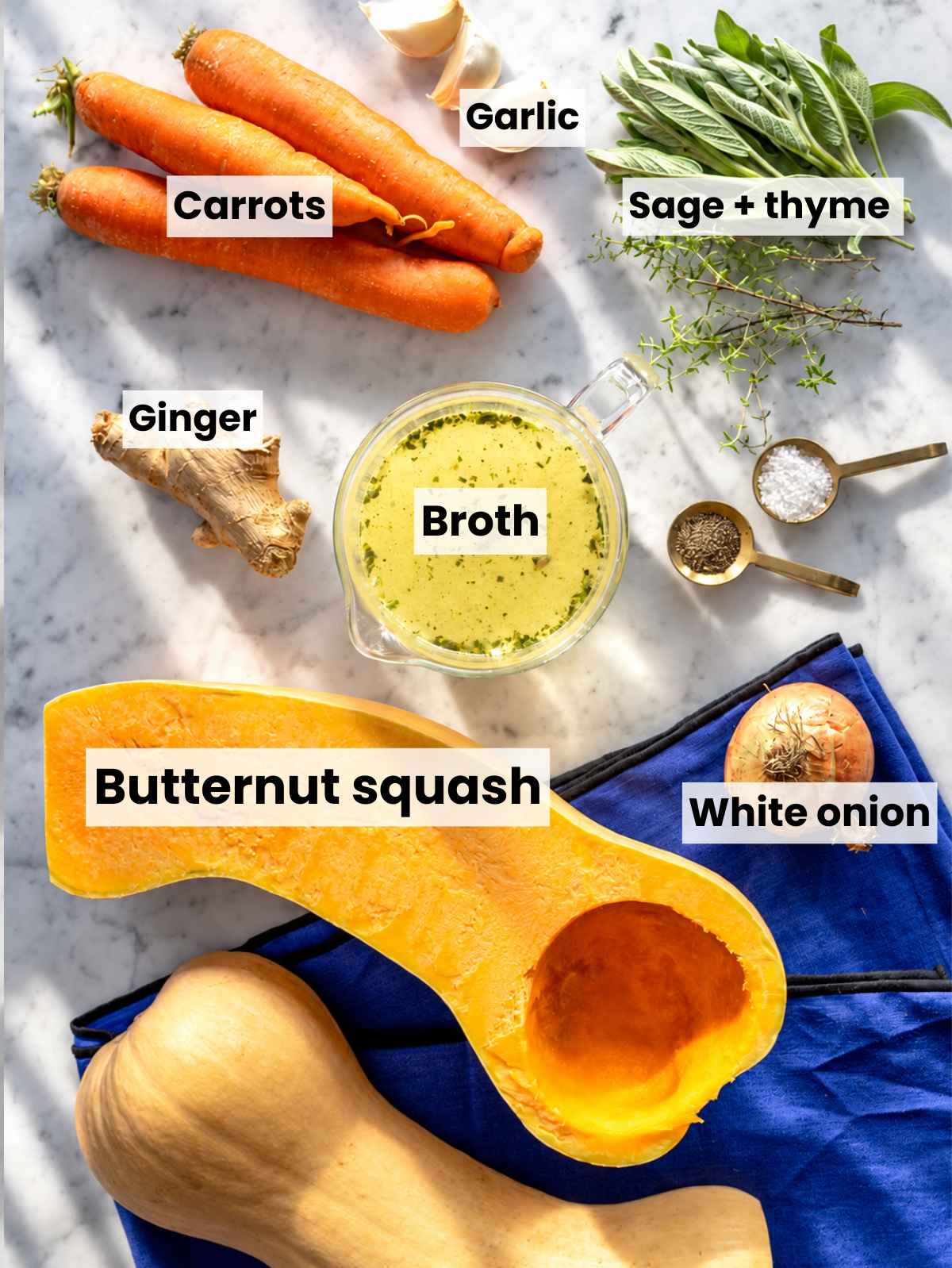 Butternut squash, carrots, onion, garlic, herbs, oil, and broth on marble.