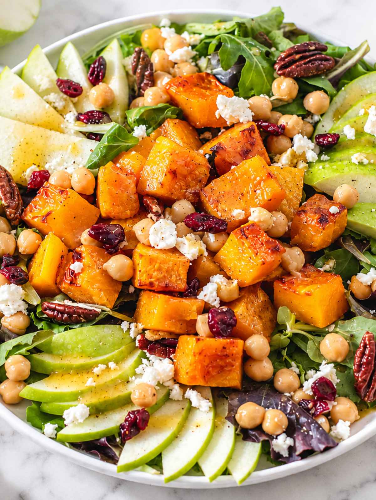 Close-up of roasted squash, glossy chickpeas, apple, feta, and greens.