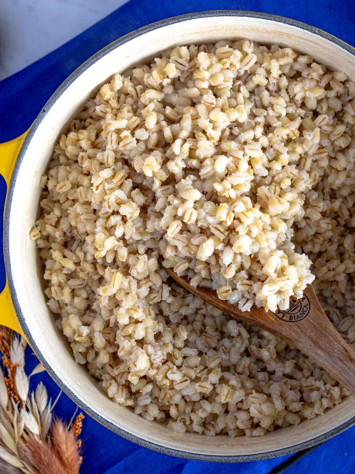 cooked barley in a yellow pot with a wooden spoon