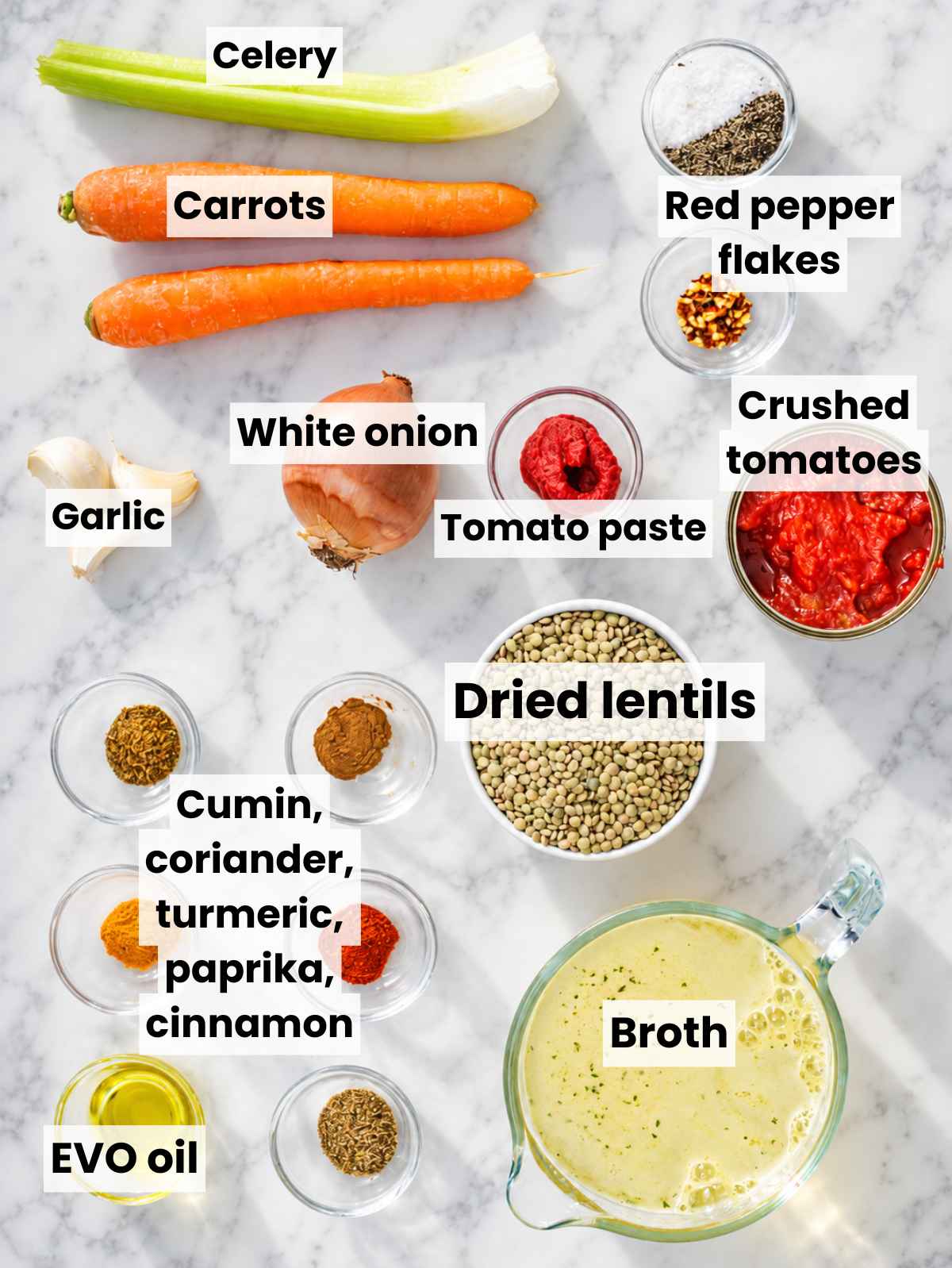 Lentils, vegetables, spices, tomatoes, broth, lemon, and herbs arranged on marble.