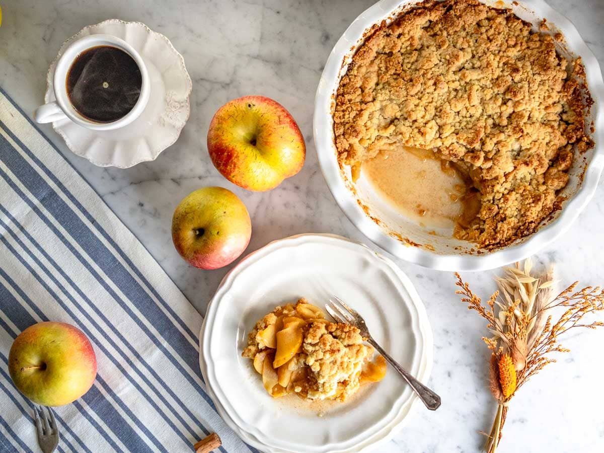 Apple crumble with a portion on a white plate and a cup of coffee