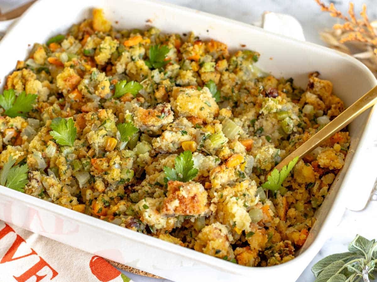 Cornbread stuffing in a white casserole with a golden spoon