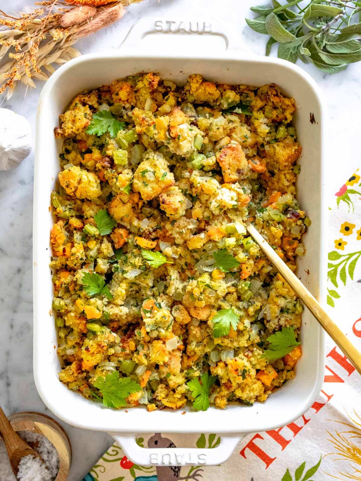 Cornbread stuffing in a white casserole with a golden spoon