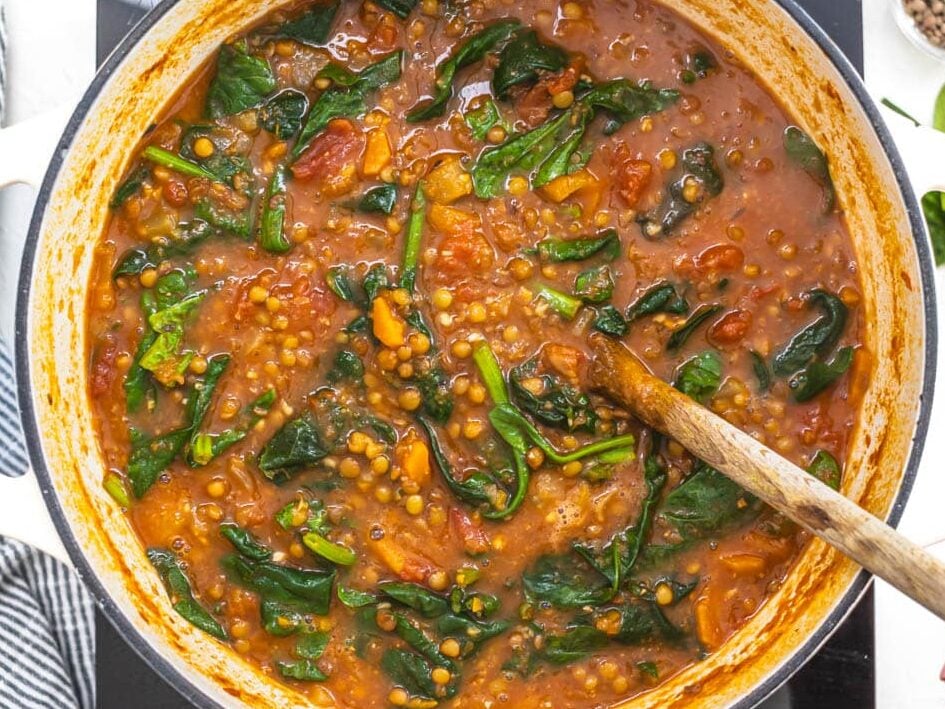 hand holding a wooden spoon and stirring spinach into a soup