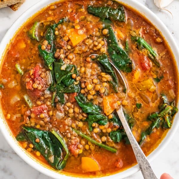 Hearty lentil vegetable soup with colorful vegetables, spinach, herbs, and olive oil.