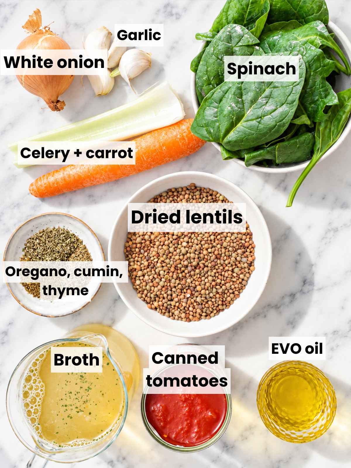 Lentils, vegetables, tomatoes, spinach, herbs, broth, and olive oil on marble.
