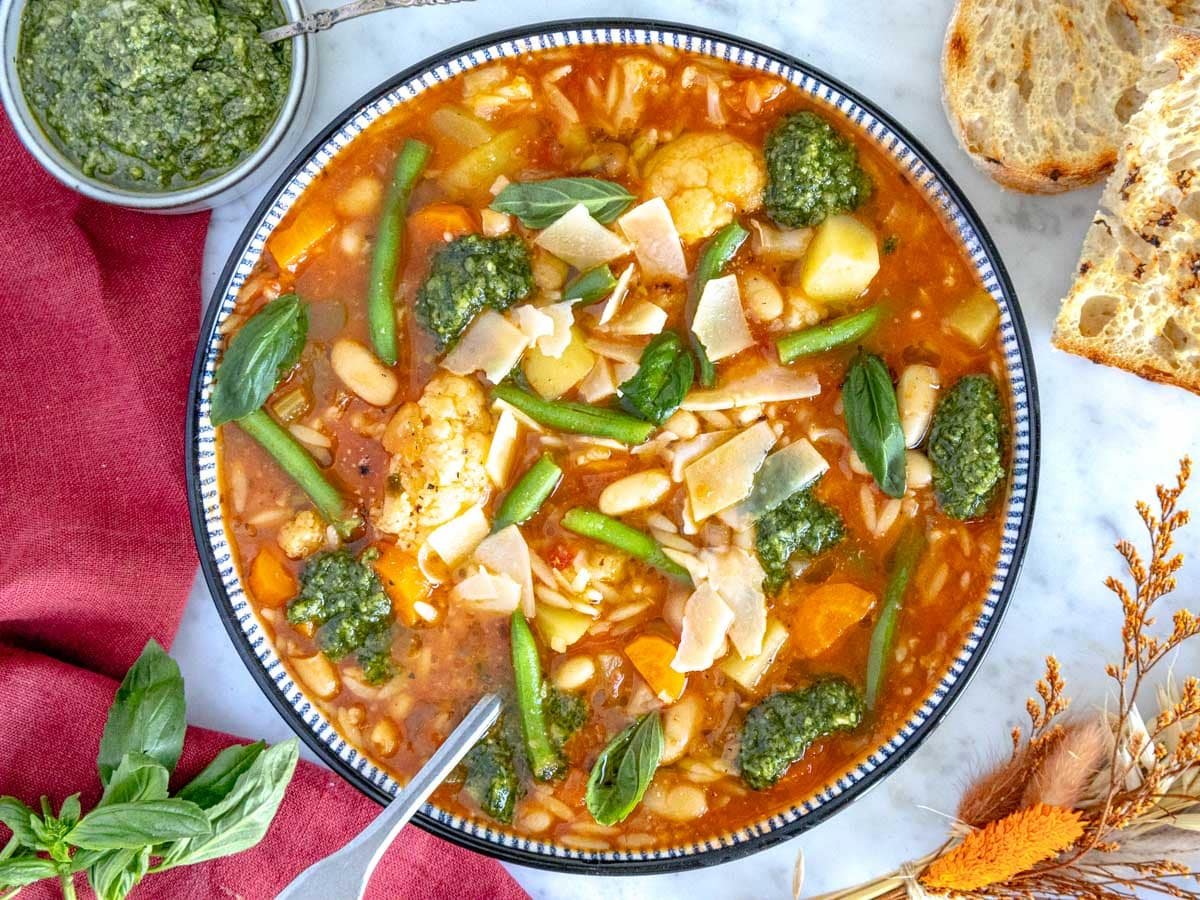 Comforting vegetable soup with spoon, pesto, and parmesan.