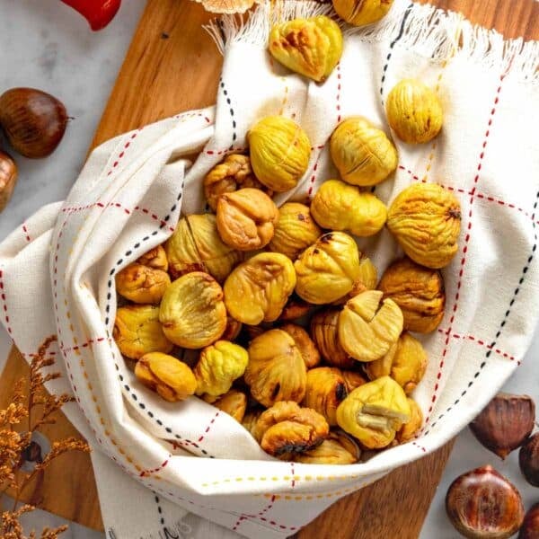 Roasted chestnuts wrapped in a kitchen cloth on a cutting board.