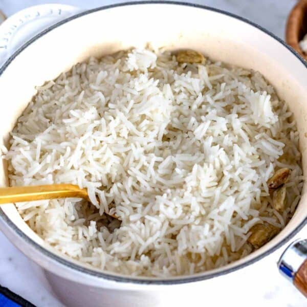 fluffy basmati rice in a pot with a golden spoon and cardamom seeds.