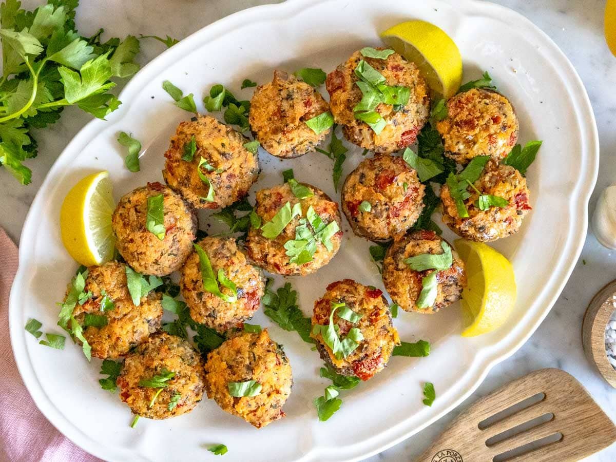 stuffed mushrooms on a white serving platter with lemon and parsley