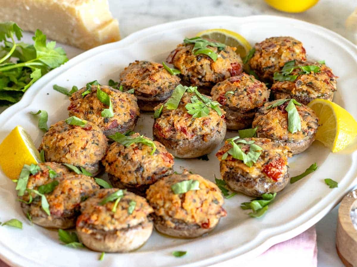 stuffed mushrooms on a white serving platter with lemon wedges