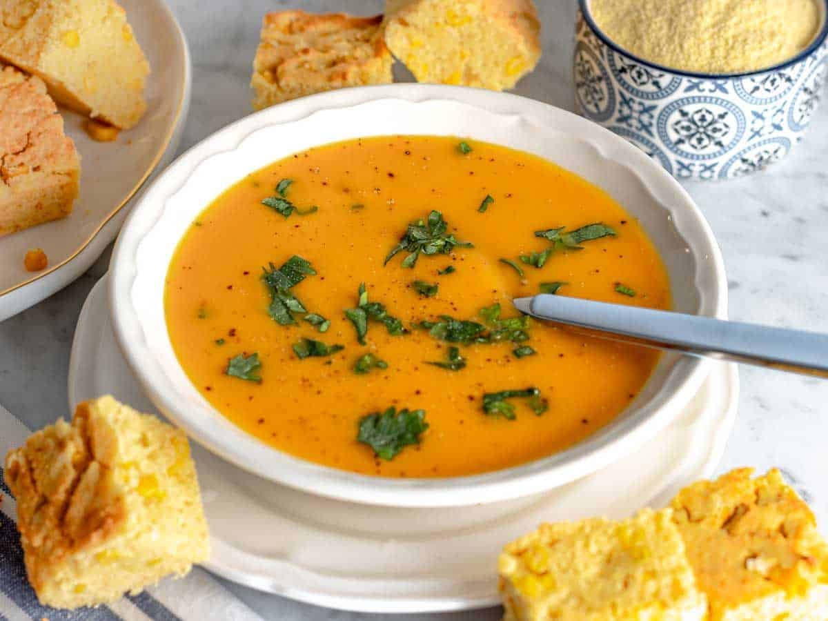 butternut squash soup with parsley and vegan cornbread in a white bowl