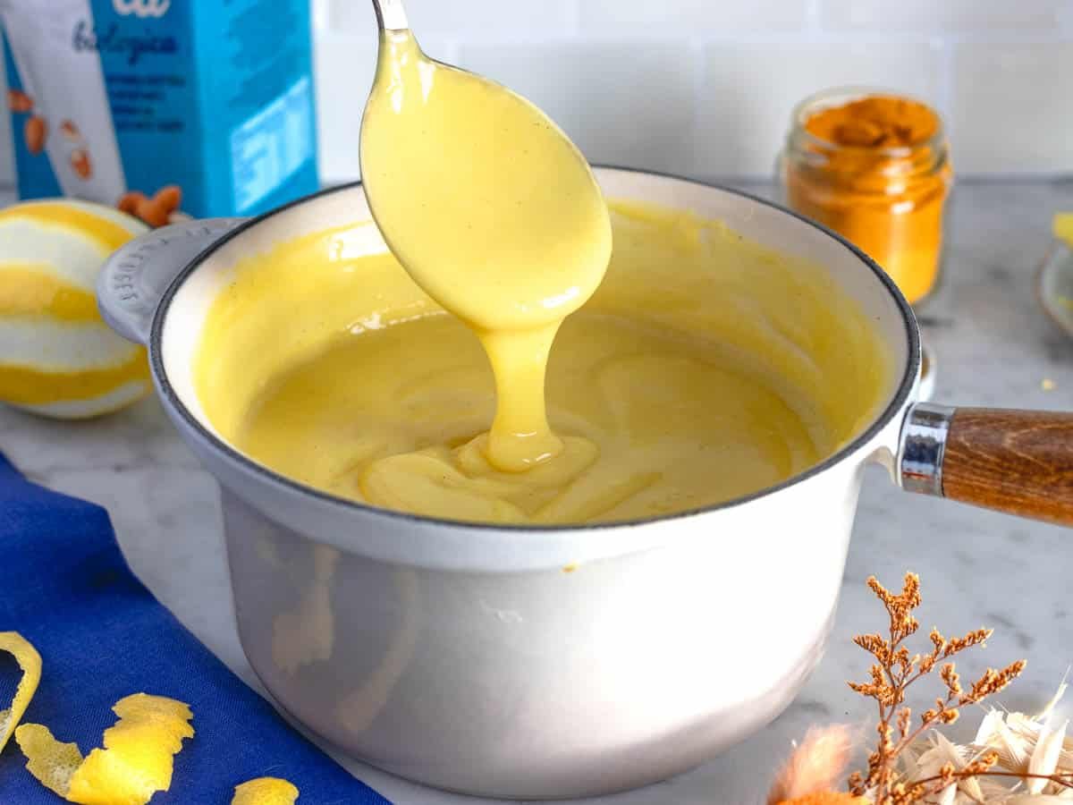 A spoonful of vegan custard in a white sauce pan.