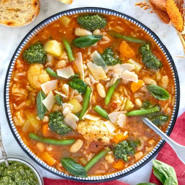 vegetable soup in a blue bowl with pesto and a spoon