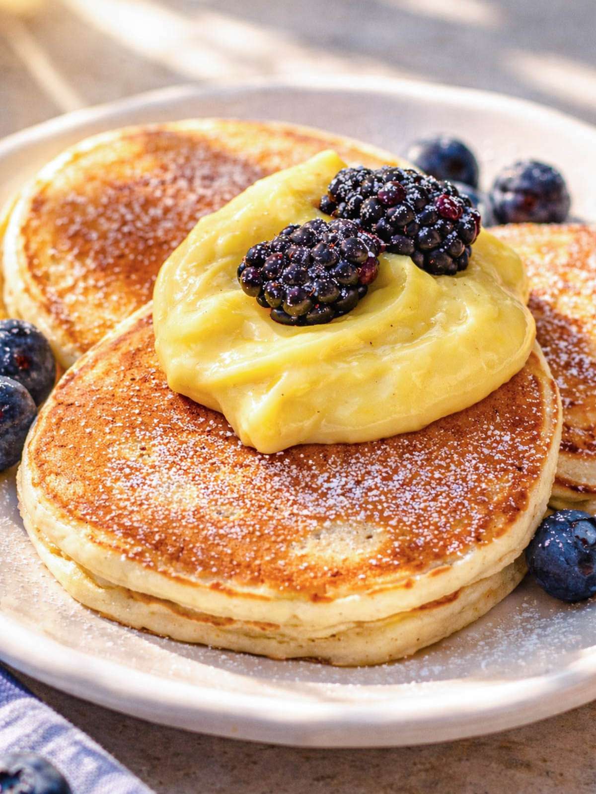 Close up of fluffy egg-free pancakes topped with berries and egg-free custard.