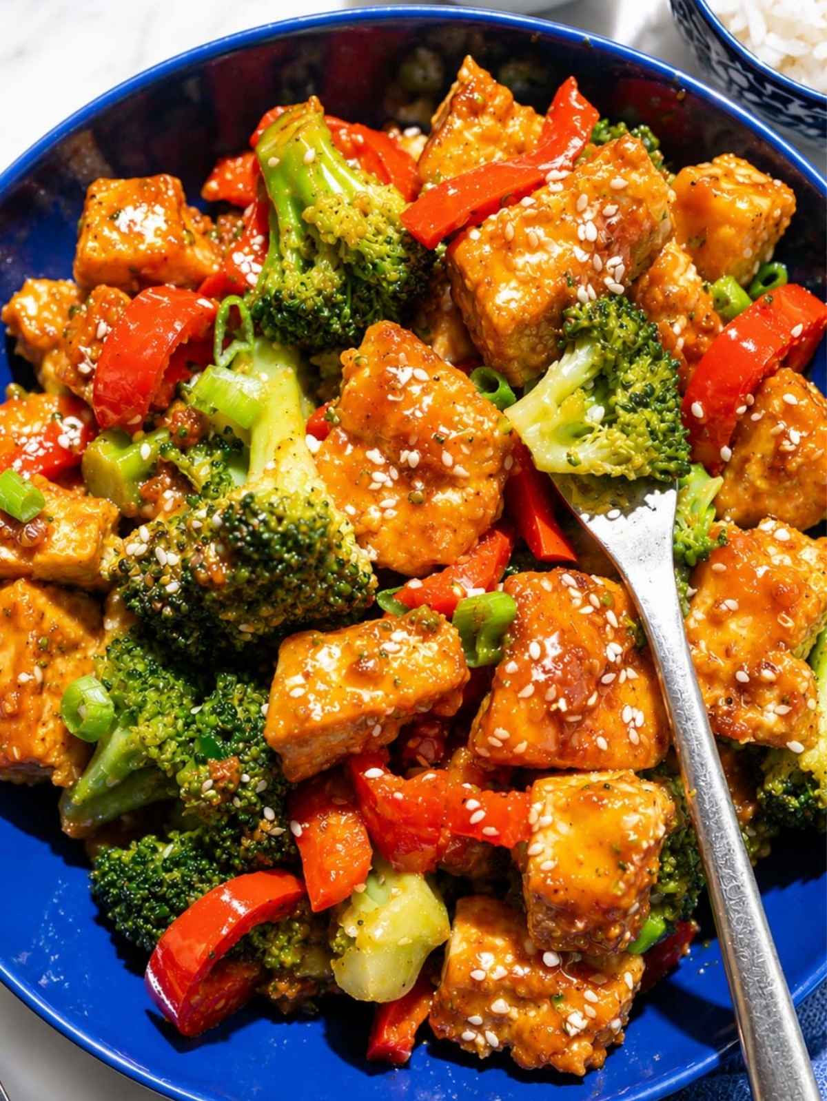 Close-up of glossy orange tofu with broccoli, green onions, and sesame seeds.