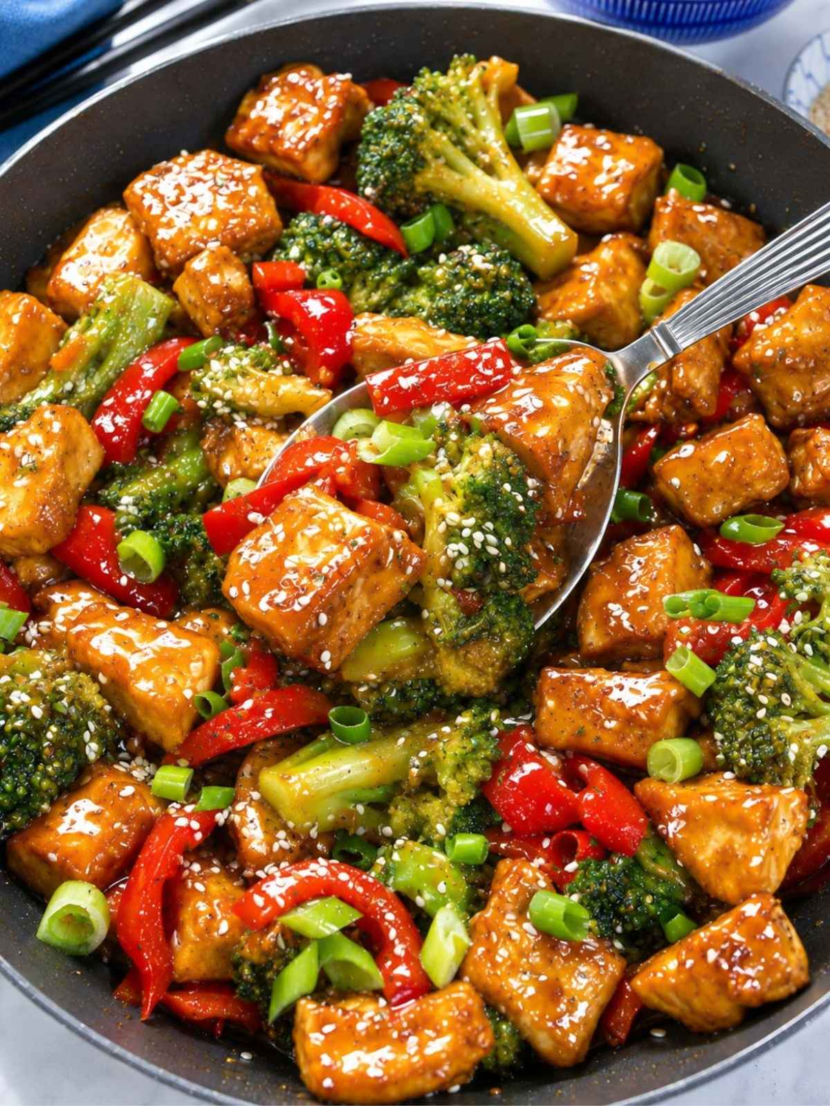 Glossy orange tofu with broccoli and red pepper served in a skillet.