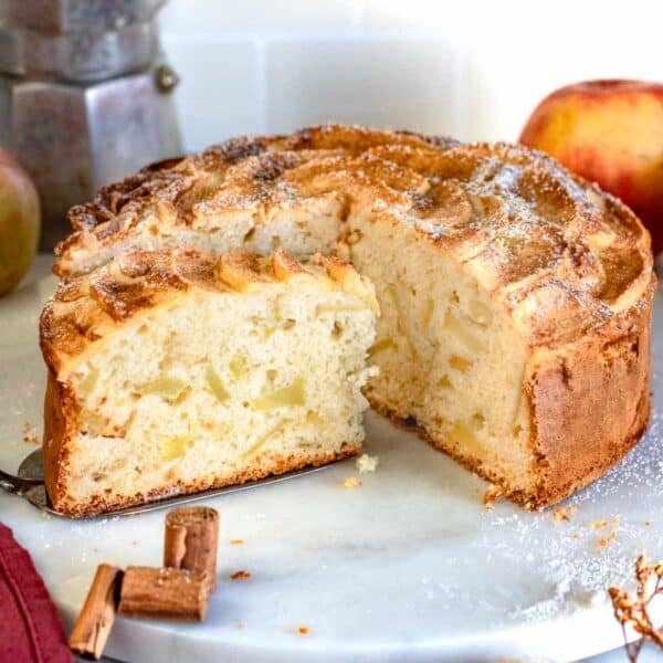 Italian apple cake with apple pieces and a slice on a serving platter.