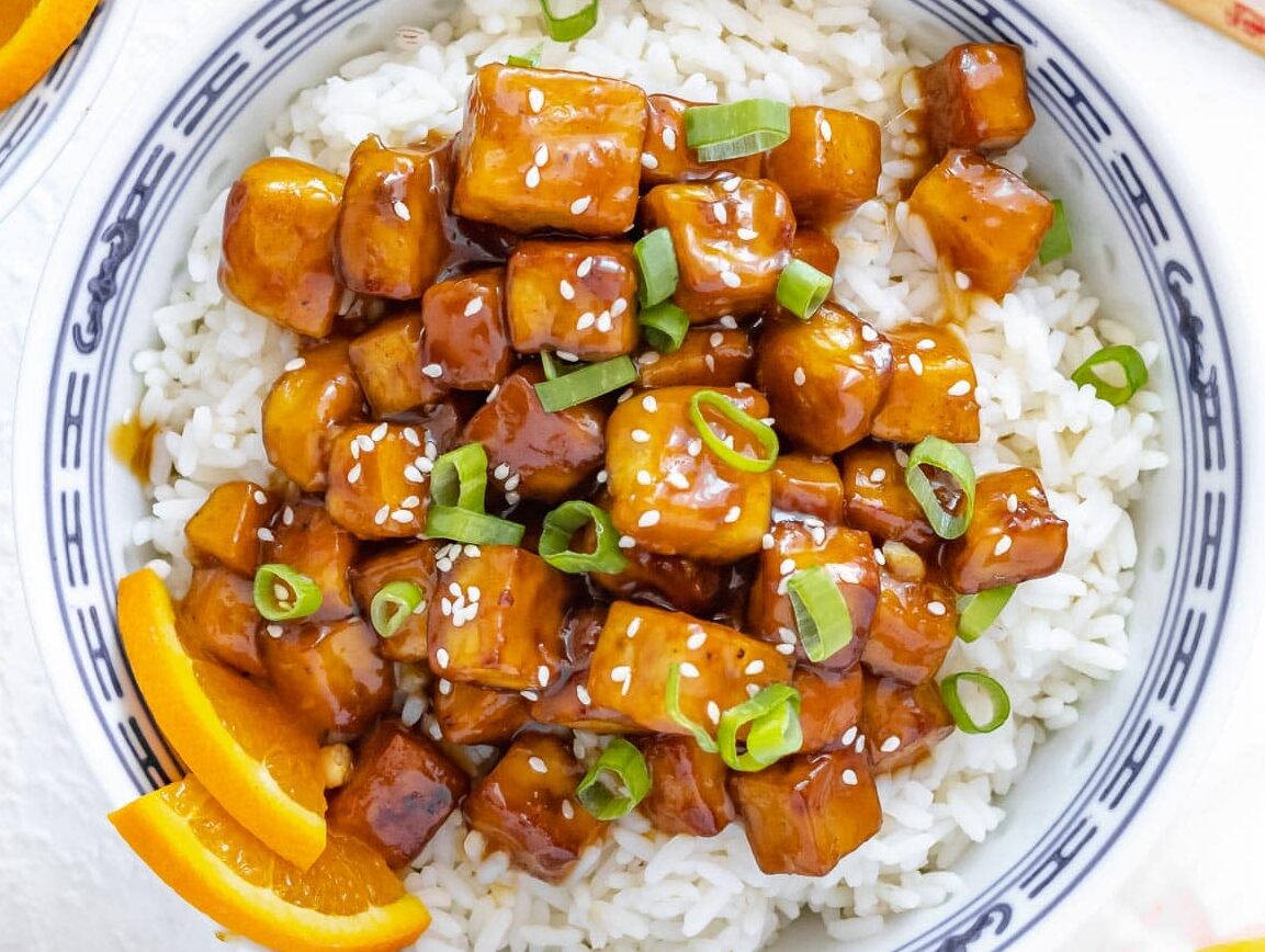 orange tofu with rice and green onions in a bowl