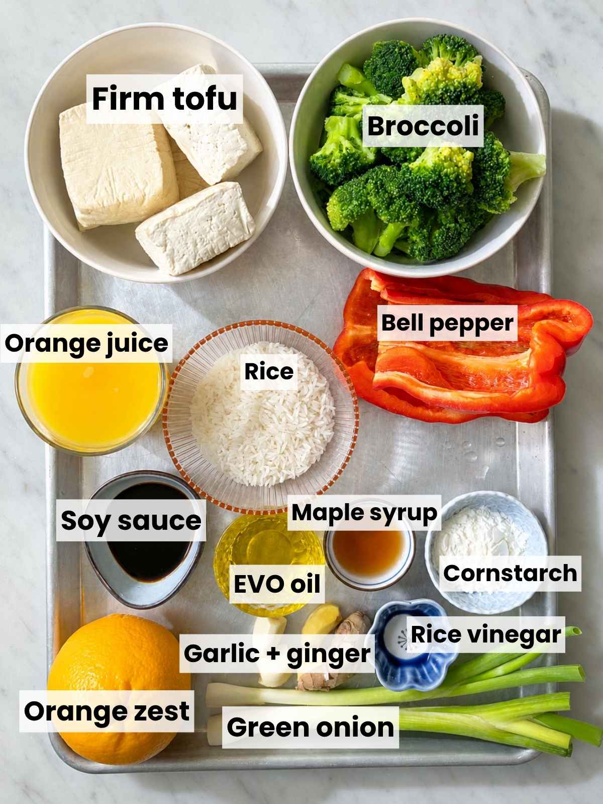 Tofu, broccoli, red pepper, orange, rice, and seasonings on white marble.