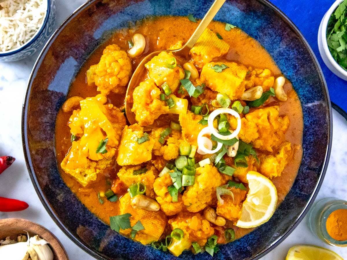 Tofu curry in a blue bowl with scallions and cashews.