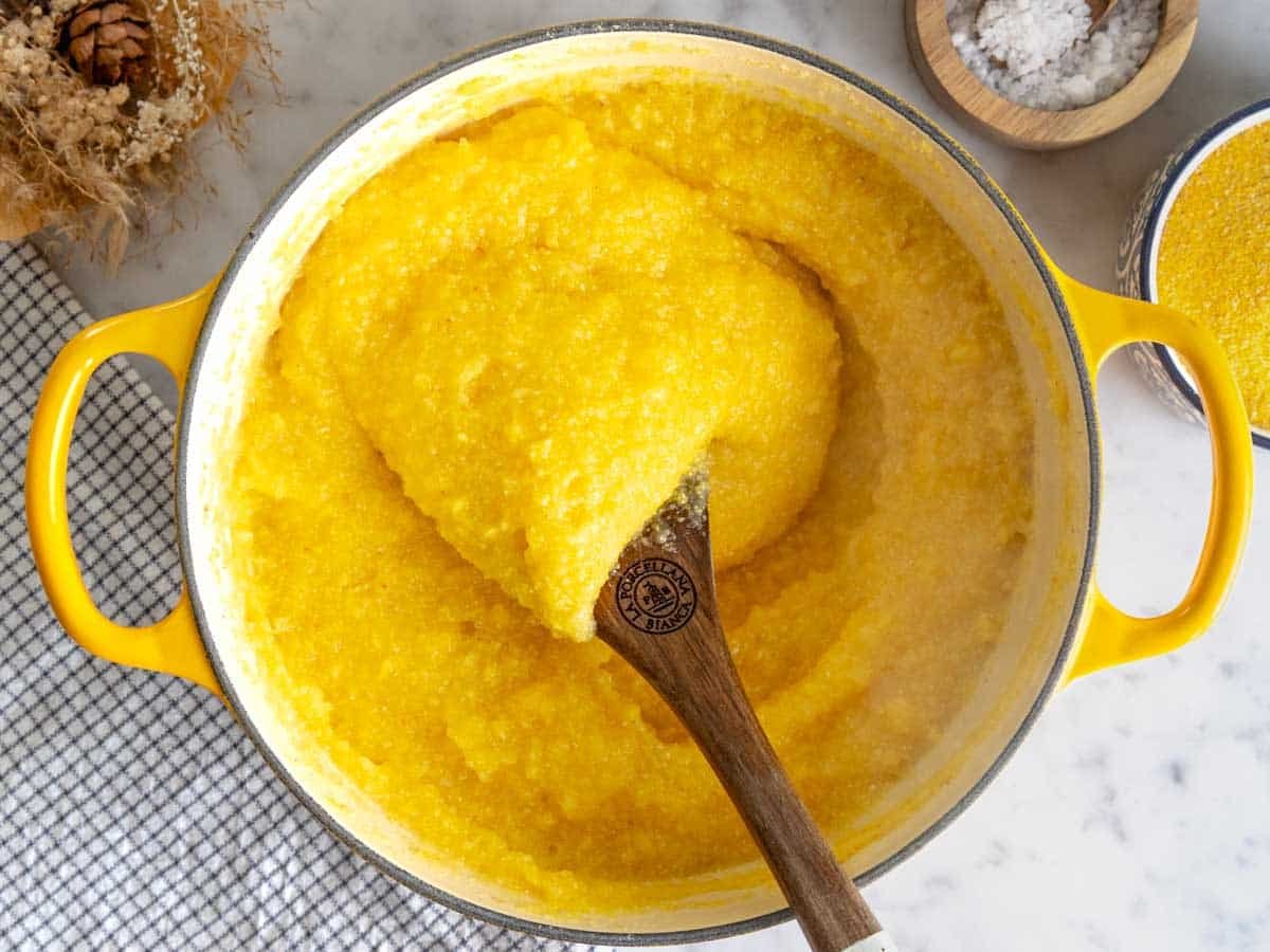 Polenta in a pot stirred with a wooden spoon.