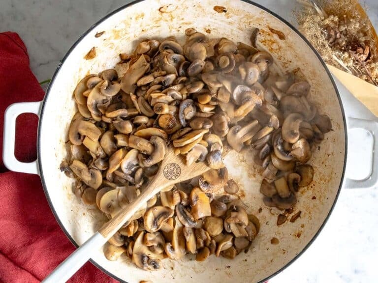 sauteed mushrooms in a white skillet with a wooden spoon