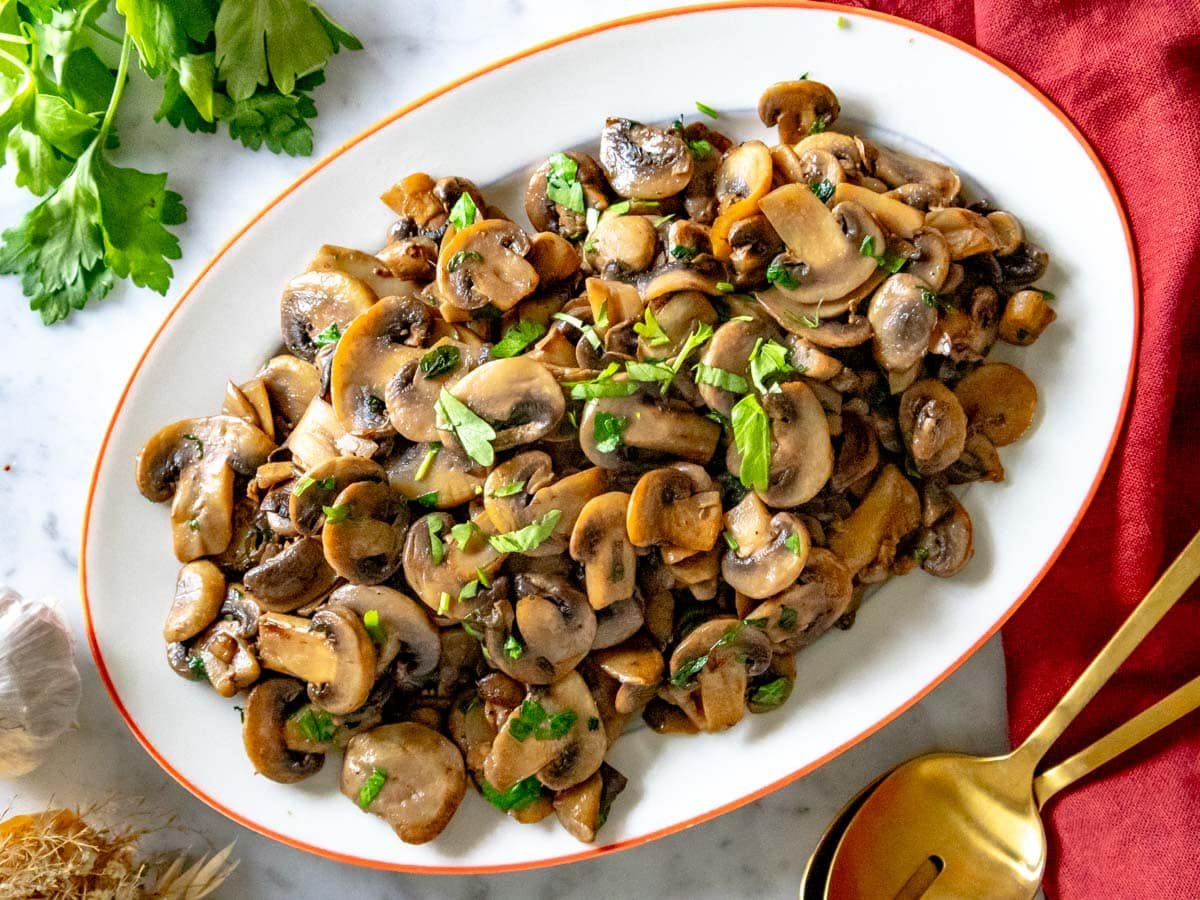 sauteed mushrooms on an oval platter and a red cloth