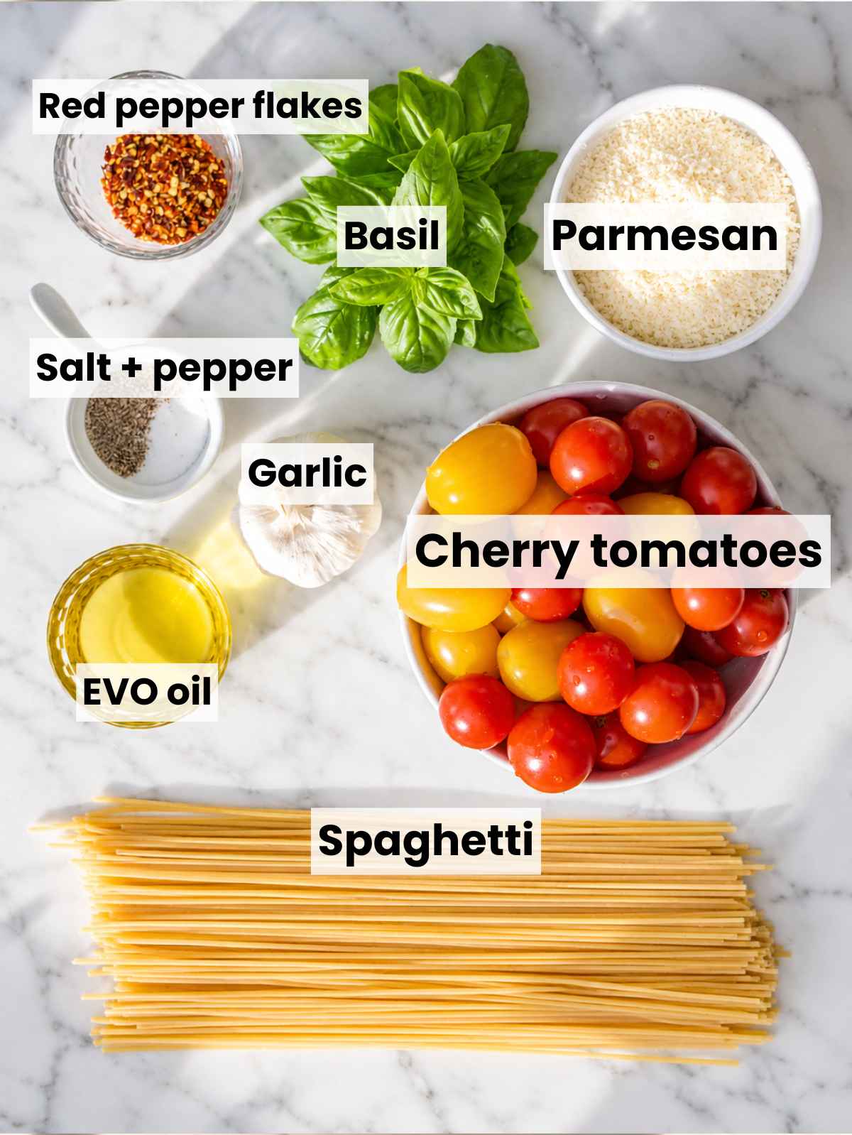 Cherry tomato pasta ingredients arranged on marble in natural window light.