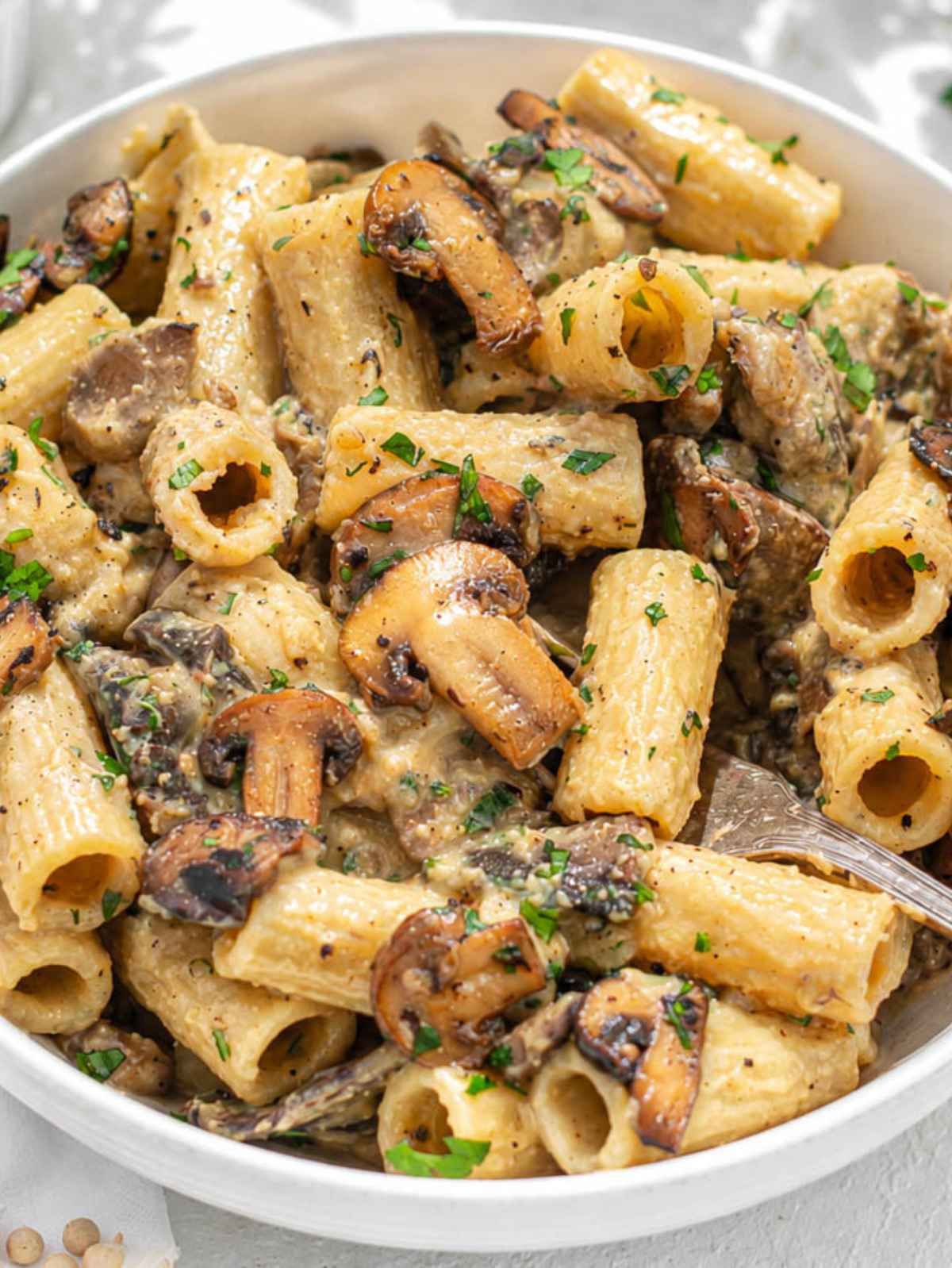 Close-up of creamy hummus pasta with mushrooms, parsley, and grated Parmesan