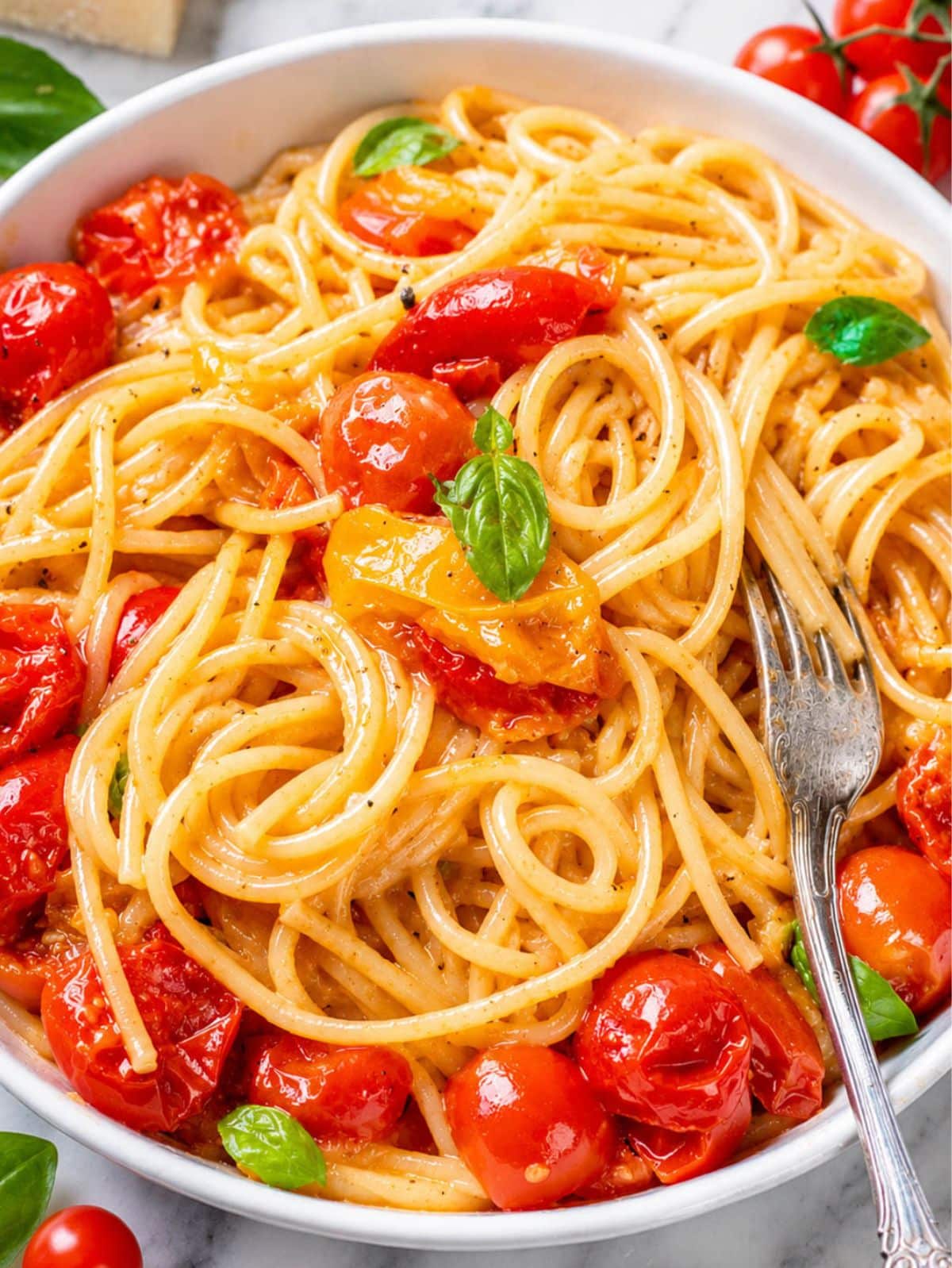 Close-up of glossy spaghetti with burst cherry tomatoes and Parmesan.