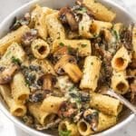Hummus pasta with a fork and browned mushrooms, parsley, Parmesan, and black pepper.